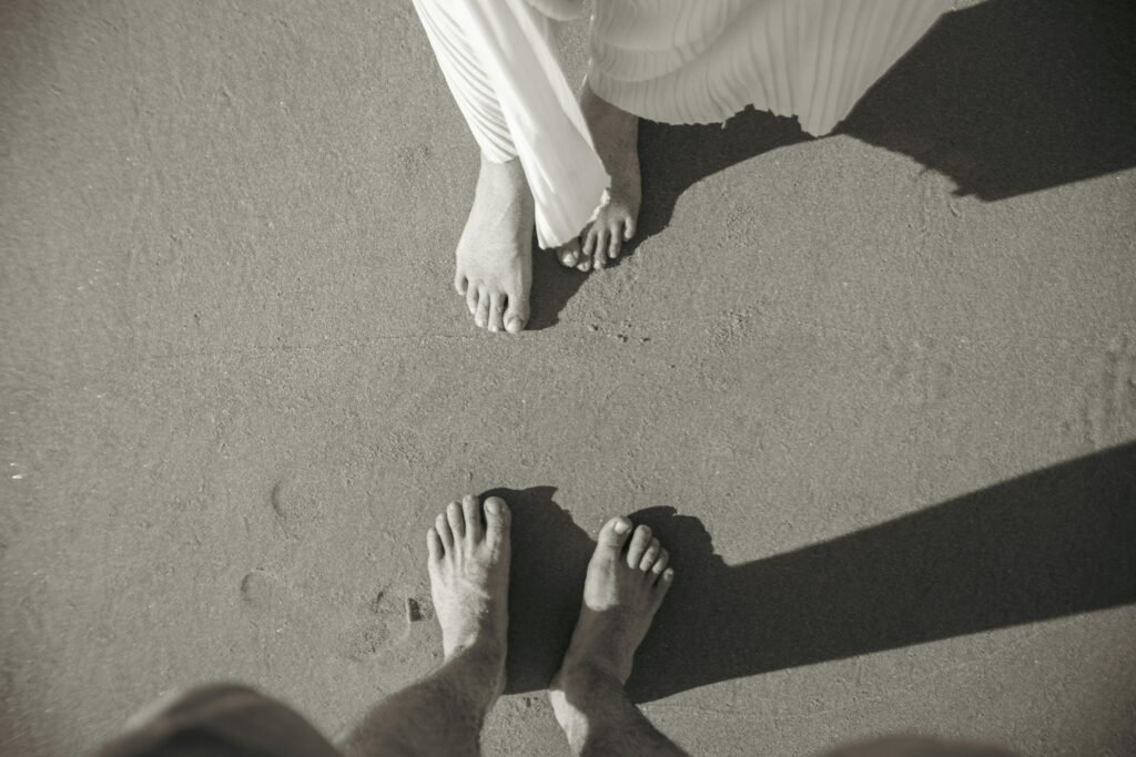 Artistic black and white image of a couple's feet on a sandy beach, capturing a romantic moment.